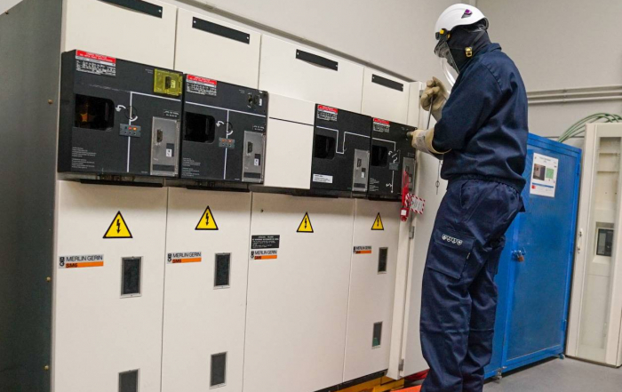 Técnico eléctrico con equipo de protección trabajando en celda de alta tensión.