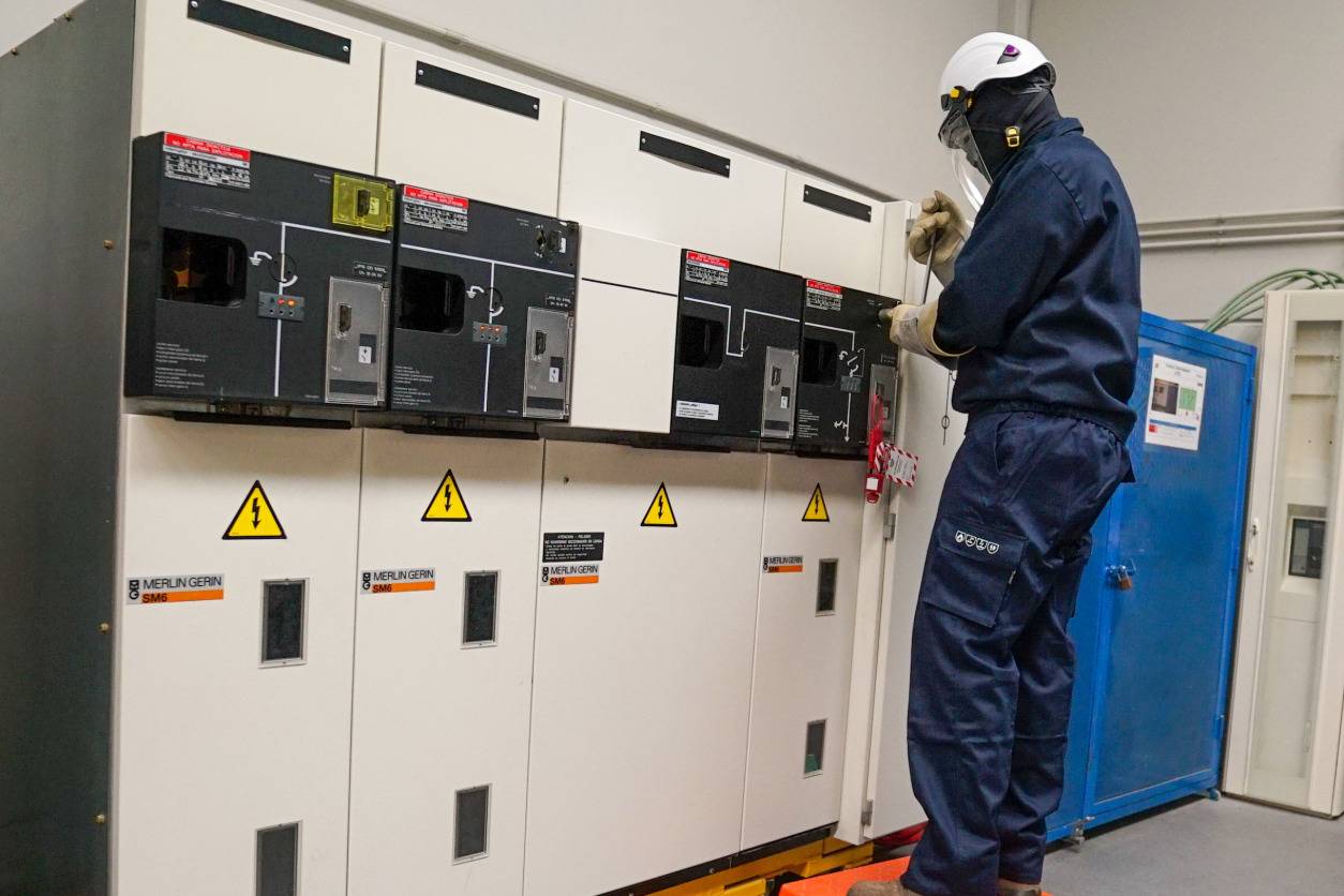 Técnico eléctrico con equipo de protección trabajando en celda de alta tensión.